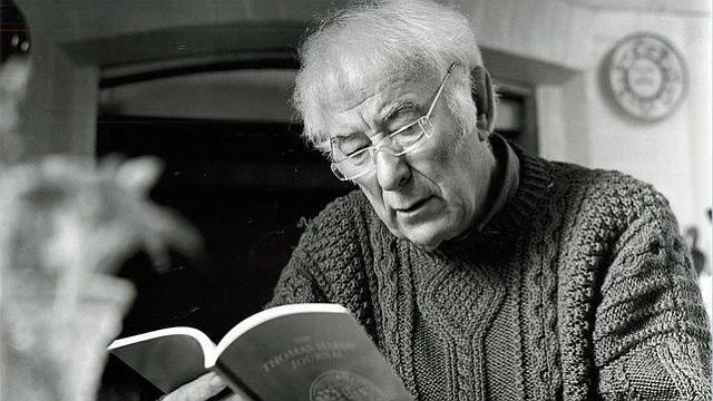 Seamus Heaney reading a book with glasses on. black and white picture